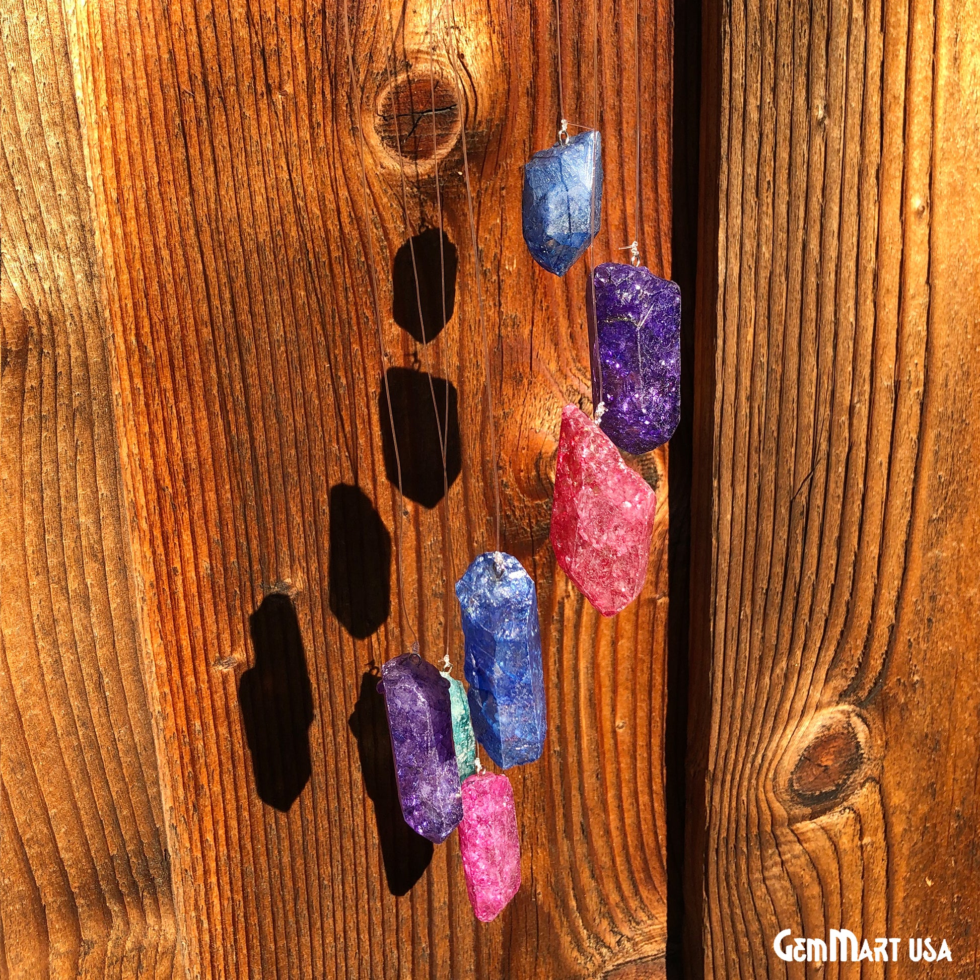 A wind chime made of rainbow-colored quartz stones hanging against a wooden background.
